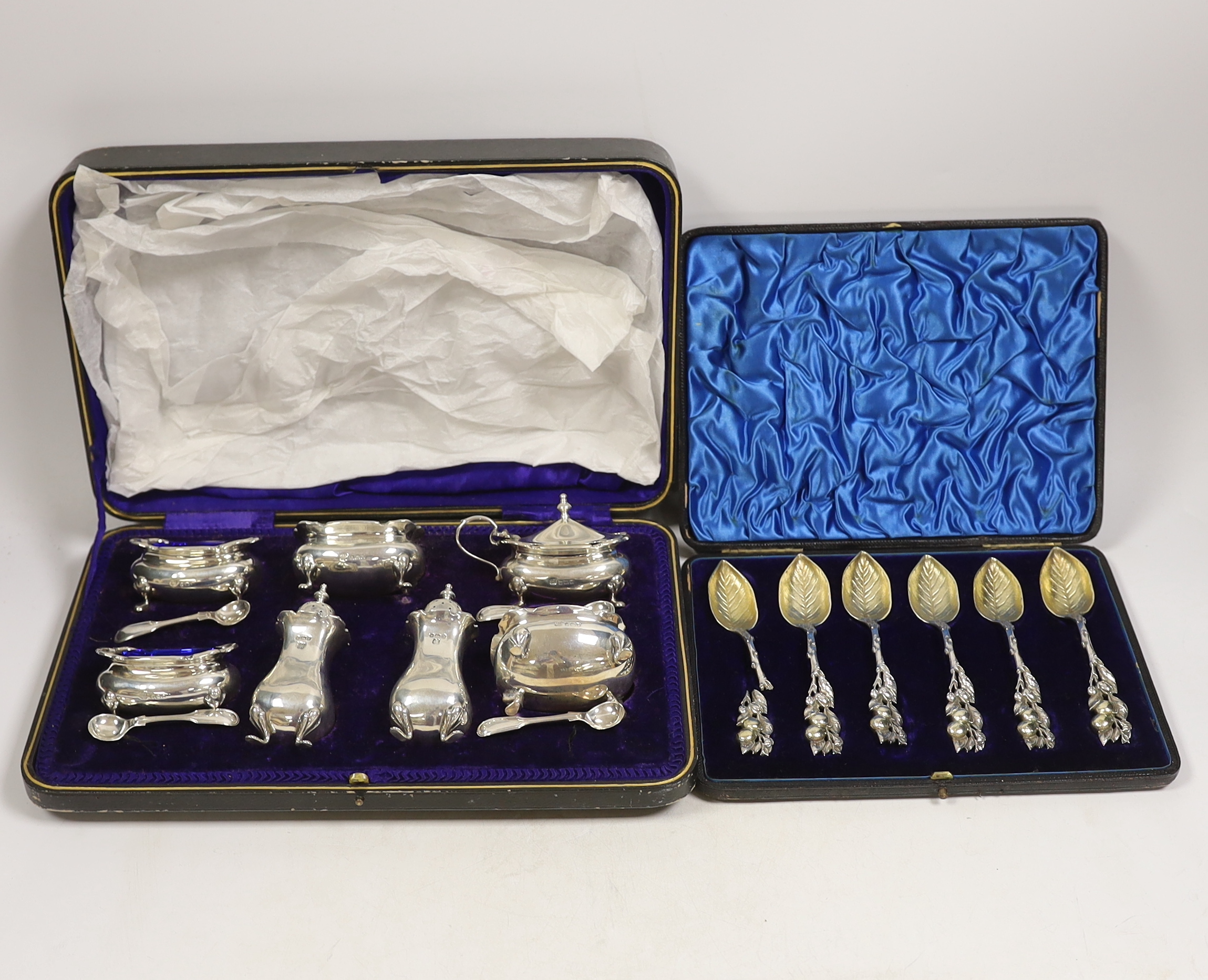 An Edwardian cased silver seven piece condiment set with four matching spoons, Hukin & Heath, Sheffield, 1908, together with an American cased set of parcel gilt sterling grapefruit spoons.